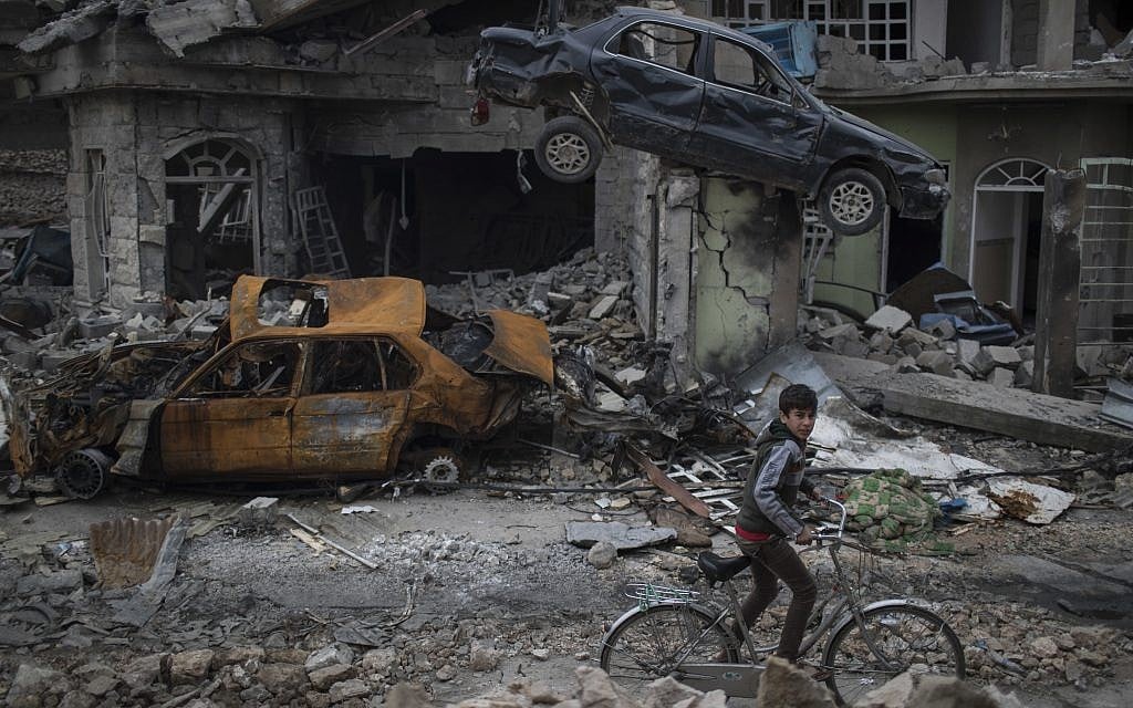 A boy rides his bike past destroyed cars and houses in a neighborhood recently liberated by Iraqi security forces on the western side of Mosul, Iraq, March 19, 2017. (AP Photo/Felipe Dana)