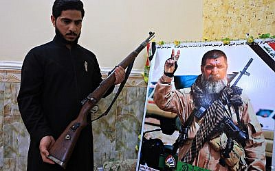 In this Tuesday, Dec. 5, 2017 photo, Talib, the son of Iraqi sniper Ali Jayad al-Salhi, 65, a volunteer with Popular Mobilization Forces killed fighting Islamic State militants, poses with a weapon next to his father's poster in his home in Basra, Iraq. (AP Photo/Nabil al-Jurani)