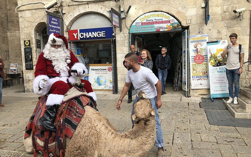 Issa Kassissieh climbs astride the camel he uses instead of a sleigh as Jerusalem Santa (Jessica Steinberg/Times of Israel)
