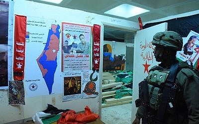 An IDF soldier stands next to what the army referred to as 'incitement materials' that were seized in overnight raids on December 14, 2017. (Israel Defense Forces)