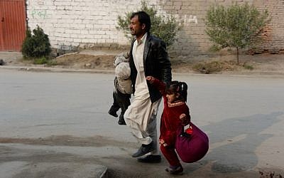 An Afghan man runs with two children near an office of the British charity Save the Children during an ongoing attack in Jalalabad on Wednesday, January 24, 2018. (AFP PHOTO/Noorullah SHIRZADA)