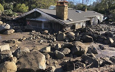 In this photo provided by Santa Barbara County Fire Department, Kerry Mann navigates the large boulders and mudflow that destroyed the home of her friend in Montecito, Calif., Wednesday, Jan. 10, 2018. The woman who lives in the home has not been seen since the early hours of Tuesday. (Mike Eliason/Santa Barbara County Fire Department via AP)