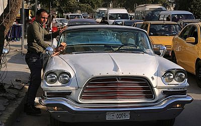 In this Wednesday, January 10, 2018 photo, a man cleans a 1952 Chrysler parked in front of owner Saad al-Nuaimi's coffee shop in the northern Azamiyah neighborhood of Baghdad, Iraq. (AP Photo/Khalid Mohammed)
