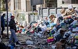 Shoppers walk past piles of garbage left by striking city workers, at Jerusalem's Mahane Yehuda Market, on January 7, 2018. (Yonatan Sindel/Flash90)