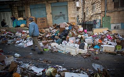 Shoppers walk past piles of garbage left by striking city workers, at Jerusalem's Mahane Yehuda Market, on January 7, 2018. (Yonatan Sindel/Flash90)