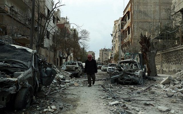 A picture taken on February 25, 2018, shows a Syrian man walking next to damaged buildings following regime air strikes in the Syrian rebel-held town of Douma, in the besieged Eastern Ghouta region on the outskirts of the capital Damascus. (AFP PHOTO / HAMZA AL-AJWEH)