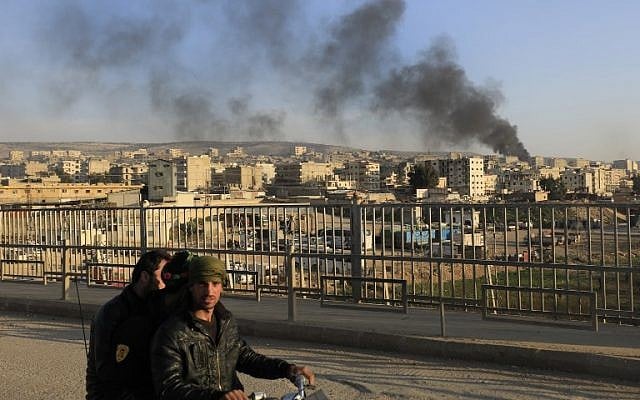 File: A picture taken in the northern town of Afrin on February 2, 2018, shows smoke from burning tires, used to block the visibility of planes, billowing in the background as people walk on a bridge. (AFP/Delil Souleiman) File: A picture taken in the northern town of Afrin on February 2, 2018, shows smoke from burning tires, used to block the visibility of planes, billowing in the background as people walk on a bridge. (AFP/Delil Souleiman)