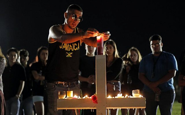 Joey Kandil, 18, a recent graduate of Marjory Stoneman Douglas High School, places a ring around a candle on one of seventeen crosses, after a candlelight vigil for the victims of the Wednesday shooting at the school, in Parkland, Florida., February 15, 2018. (AP Photo/Gerald Herbert)