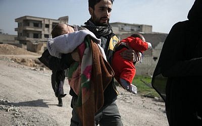 A Syrian civil defense volunteer carries children, as he helps them try to flee their homes in the town of Hamouria in Syria's besieged eastern Ghouta region on March 4, 2018, following reported airstrikes. (AFP PHOTO / ABDULMONAM EASSA)