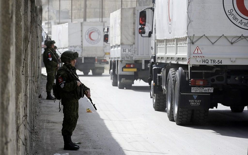 Russian soldiers stand guard as Syrian Arab Reb Crescent trucks carrying aid drive through the al-Wafideen checkpoint on the outskirts of Damascus towards the rebel-held Eastern Ghouta region on March 5, 2018. (AFP Photo/Louai Beshara)