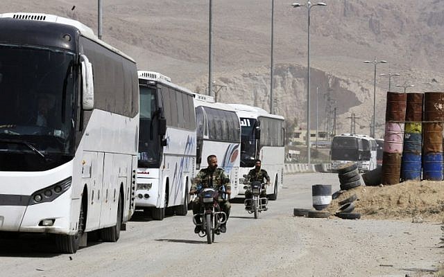 Syrian regime forces drive motorbikes past buses waiting at the entrance of Harasta in Eastern Ghouta, on the outskirts of Damascus, on March 22, 2018, after a deal was struck with the rebels in the area to evacuate the town. (AFP PHOTO / Louai Beshara) Syrian regime forces drive motorbikes past buses waiting at the entrance of Harasta in Eastern Ghouta, on the outskirts of Damascus, on March 22, 2018, after a deal was struck with the rebels in the area to evacuate the town. (AFP PHOTO / Louai Beshara)