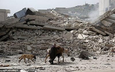 A picture taken on March 22, 2018, shows a man walking with a loaded donkey and followed by a dog past the rubble of a destroyed building in the northwestern Syrian city of Afrin. (AFP PHOTO / Nazeer al-Khatib)