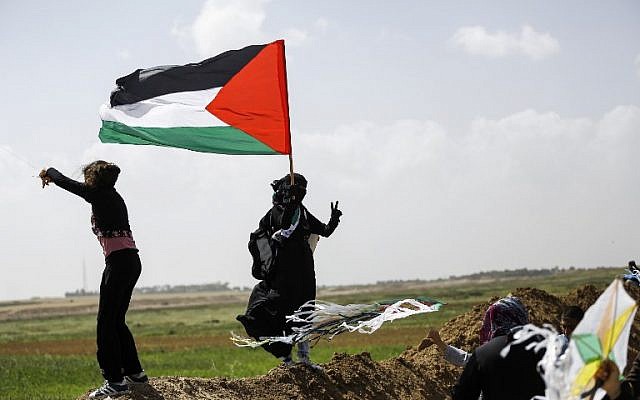 A Palestinian woman wearing niqab (full face veil) flashes the victory gesture while holding a Palestinian flag as others fly kites during a demonstration ahead of Land Day, at a tent city near the border with Israel east of Gaza City on March 29, 2018. (AFP PHOTO / MOHAMMED ABED) A Palestinian woman wearing niqab (full face veil) flashes the victory gesture while holding a Palestinian flag as others fly kites during a demonstration ahead of Land Day, at a tent city near the border with Israel east of Gaza City on March 29, 2018. (AFP PHOTO / MOHAMMED ABED)