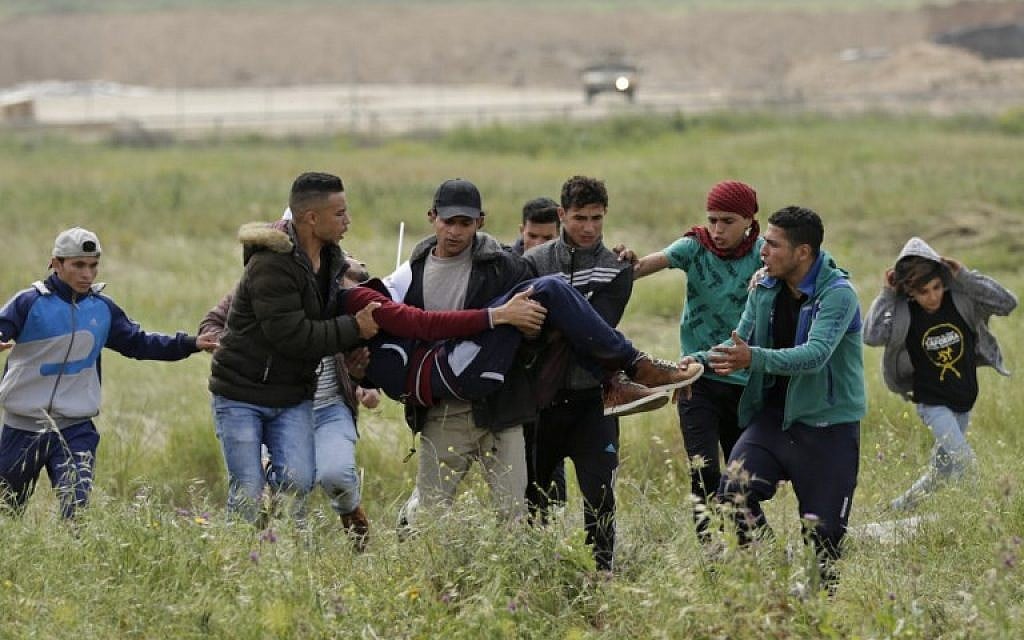 An injured Palestinian youth is carried by other protesters as they flee during clashes after a demonstration near the border with Israel east of Gaza City commemorating Land Day, March 30, 2018 (AFP/ MAHMUD HAMS)