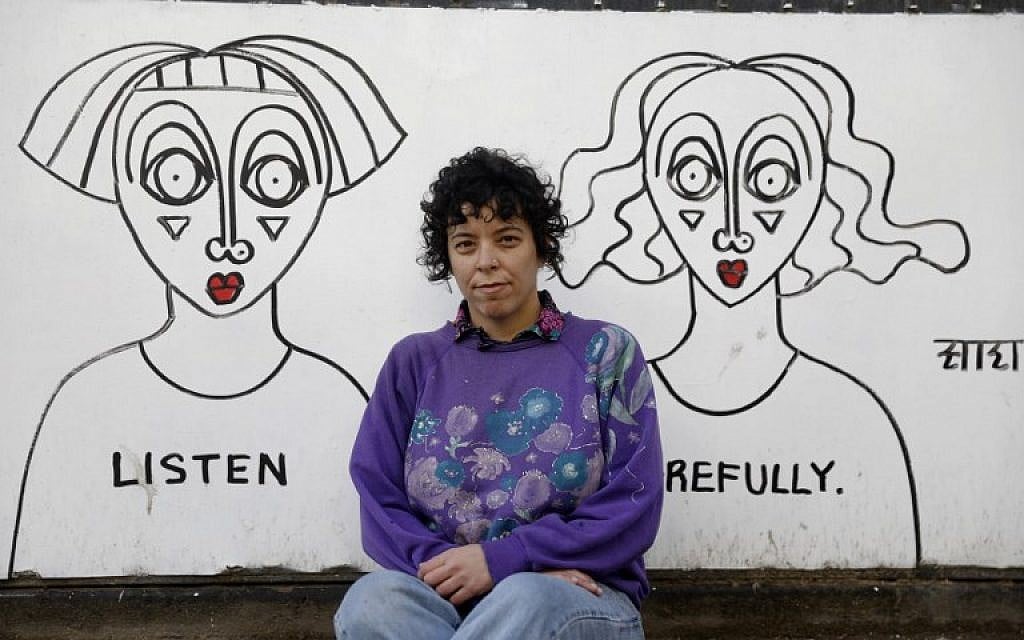 Israeli-born New York-based street artist Sara Erenthal sits in front of one of her murals in Tel Aviv on January 28, 2018. (AFP Photo/Menahem Kahana)