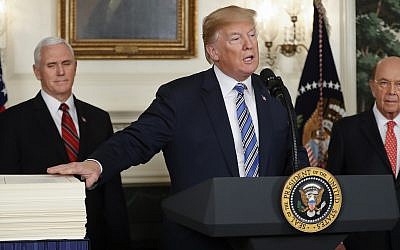 President Donald Trump reaches to touch a copy of the $1.3 trillion spending bill as he speaks in the Diplomatic Room of the White House in Washington, Friday, March 23, 2018, as Vice President Mike Pence, left, and Commerce Secretary Wilbur Ross watch. (AP Photo/Pablo Martinez Monsivais)