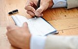 Illustrative: A man writes a check (PeopleImages/Getty Images via JTA)