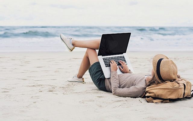 Illustrative woman using laptop on beach (Poike, iStock by Getty Images)