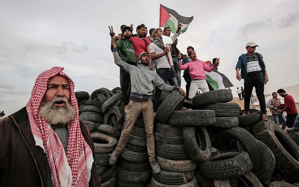 Palestinian protesters wave their national flag on a tire pile near the border with Israel, east of Khan Yunis, in the southern Gaza Strip, on April 3, 2018, ( AFP PHOTO / SAID KHATIB)