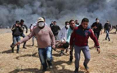 Illustrative: An injured Palestinian protester is carried by fellow demonstrators during clashes with Israeli security forces near the border with Israel, east of Khan Younis, in the southern Gaza Strip, on April 6, 2018. (AFP/Said Khatib)