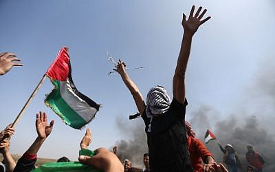 Palestinian demonstrators wave their national flag and shouts slogans against Israeli security forces during a protest on the Israel-Gaza border in the northern Gaza Strip on April 6, 2018. (AFP/Mohammed Abed)