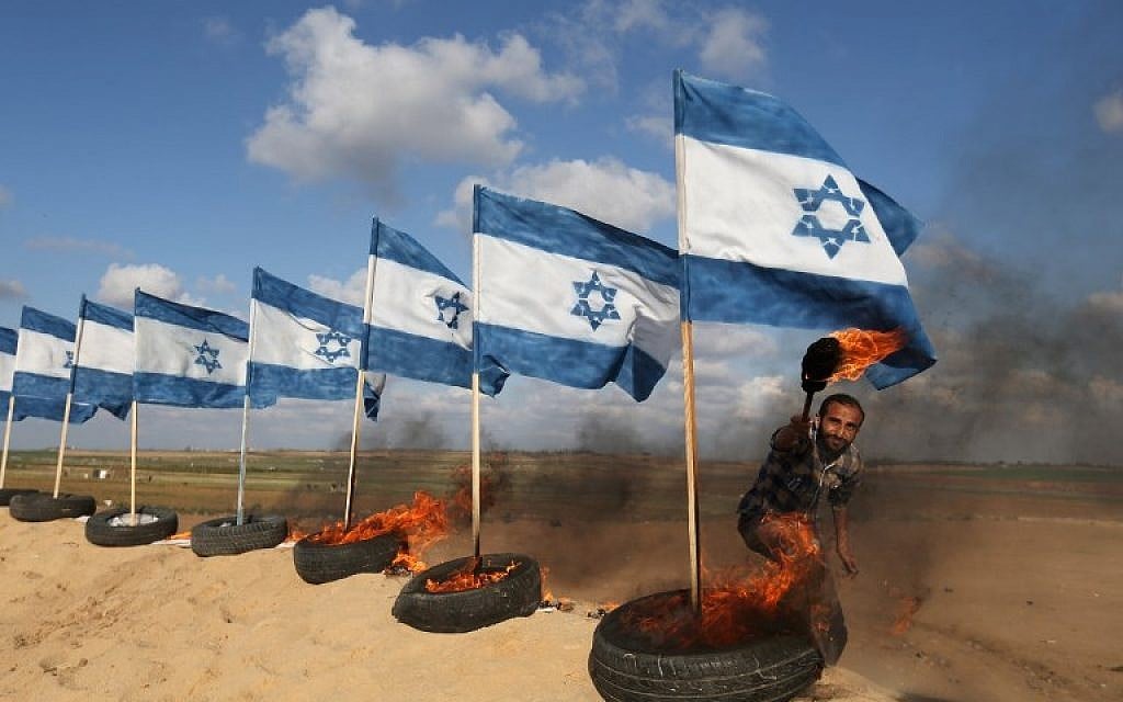 A Palestinian protestor prepares to set fire on Israeli flags on April 10, 2018 at the site of protests on the Israel-Gaza border east of Jabalia in the northern Gaza Strip. (AFP PHOTO / Mohammed ABED)