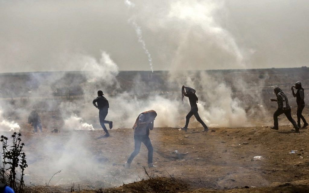 Palestinians take cover from tear gas smoke during clashes with Israeli security forces near the border fence with Israel, east of Gaza City in the central Gaza Strip on April 13, 2018.(AFP PHOTO / MAHMUD HAMS)