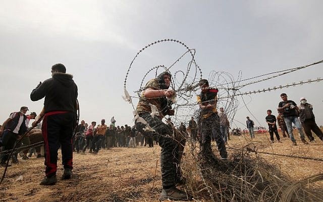 Illustrative. Palestinians pull barbed wire from the border fence with Israel during weekly Friday clashes, in Rafah in southern Gaza Strip, on April 20, 2018. (AFP Photo/Said Khatib)