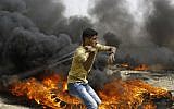 A Palestinian slings a shot by burning tires during clashes with Israeli forces across the border, east of Gaza City, in the southern Gaza Strip, on April 20, 2018. (MOHAMMED ABED / AFP)
