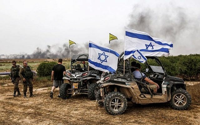 Israelis sit in parked dune buggies flying Israeli flags near IDF soldiers in the southern kibbutz of Nahal Oz on April 20, 2018, across from the border with Gaza as Palestinians take part in violent protests along the fence. (AFP Photo/Ahmad Gharabli)