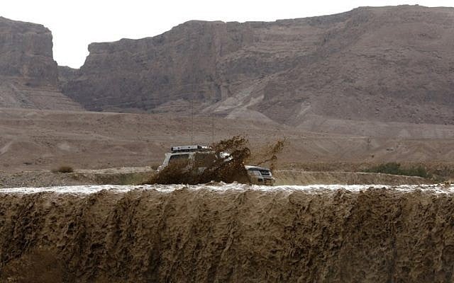 Illustrative: A car drives through flooded water running through a valley blocking the main road along the Dead Sea, near the desert fortress of Masada, following heavy rainfall on April 25, 2018. (AFP Photo/Menahem Kahana)