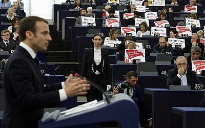 European lawmakers raise placards reading 'Stop the War in Syria' in protest against airstrikes launched by the US, Britain and France in Syria last week, as French President Emmanuel Macron delivers his speech at the European Parliament in Strasbourg, eastern France, April 17, 2018. (AP Photo/ Jean Francois Badias)