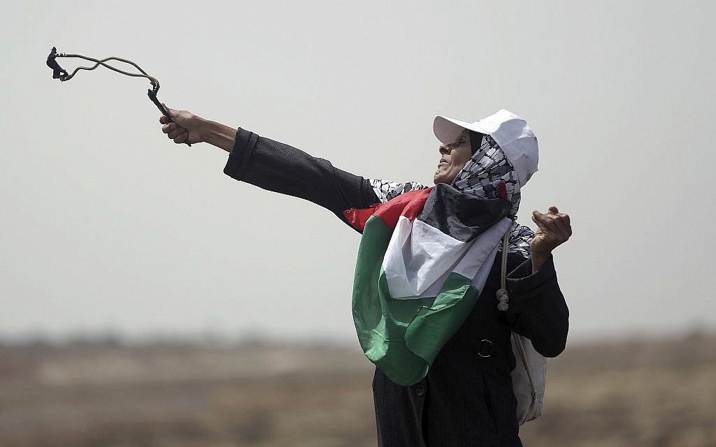 A Palestinian woman hurls stones at Israeli troops during a protest at the Gaza Strip's border with Israel, on April 20, 2018. (AP Photo/ Khalil Hamra)