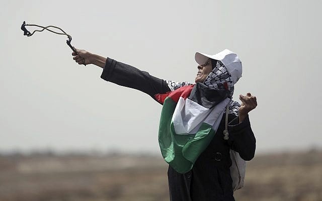 A Palestinian woman hurls stones at Israeli troops during a protest at the Gaza Strip's border with Israel, on April 20, 2018. (AP Photo/ Khalil Hamra)