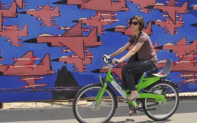 Illustrative: A young Israeli woman rides her bicycle past graffiti in Tel Aviv on May 14, 2012. (Serge Attal/Flash90)