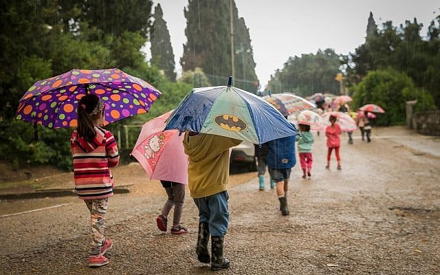 Kids take cover under umbrellas on a rainy day as they walk in Kibbutz Sarid in northern Israel on April 25, 2018. (Anat Hermony/Flash90)