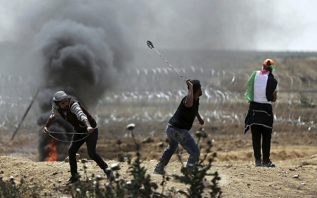 Palestinian protesters hurl stones at Israeli troops during a protest at the Gaza Strip's border with Israel, Friday, April 13, 2018. (AP Photo/Khalil Hamra)