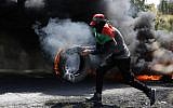 File: A Palestinian protester carries a burning tire during clashes between Palestinians and Israeli soldiers near Ramallah in the West Bank on, May 11, 2018. (AFP/Abbas Momani)