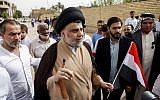 Iraqi Shiite cleric and leader Muqtada al-Sadr, center-left, shows his ink-stained index finger and holds a national flag while surrounded by people outside a polling station in the central holy city of Najaf on May 12, 2018. (Haidar Hamdani/AFP)