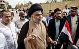 Iraqi Shiite leader Moqtada al-Sadr (C-L) shows his ink-stained index finger and holds an Iraqi flag outside a polling station in the holy city of Najaf on May 12, 2018, as the country votes in the first parliamentary election since declaring victory over the Islamic State terror group. (AFP Photo/Haidar Hamdani)