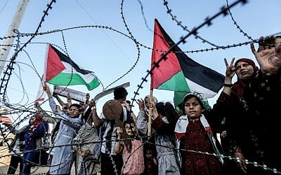 A girl raises a Palestinian flag as another Palestinian boy holds a wooden key symbolizing the return, as they stand with others before the barbed-wire marking the border between the Gaza strip and Israel east of Gaza City on May 13, 2018. (AFP/Mahmud Hams)