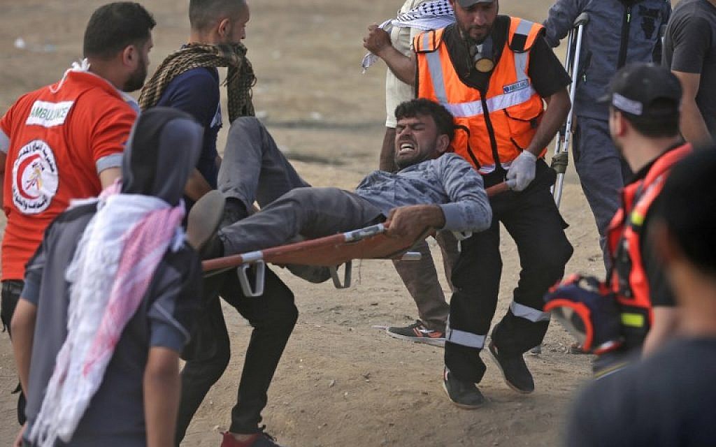 Palestinians carry a protester injured during clashes along the Gaza-Israel border, May 14, 2018 (AFP Photo/Mahmud Hams)