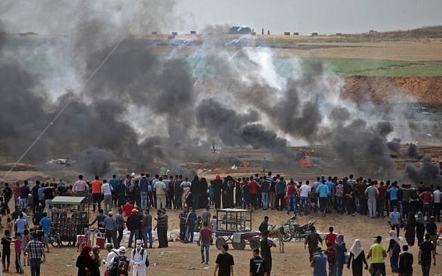 Palestinian protesters look at tear gas and smoke billowing from burning tires, east of Gaza City on May 14, 2018 (AFP PHOTO / Mohammed ABED)