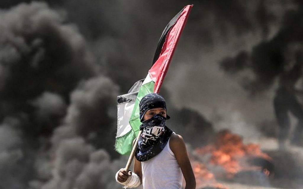 A Palestinian boy holding his national flag looks at clashes with Israeli security forces near the border between the Gaza Strip and Israel east of Gaza City on May 14, 2018 (AFP PHOTO / MAHMUD HAMS) A Palestinian boy holding his national flag looks at clashes with Israeli security forces near the border between the Gaza Strip and Israel east of Gaza City on May 14, 2018 (AFP PHOTO / MAHMUD HAMS)