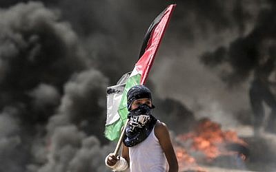 A Palestinian boy holding his national flag looks at clashes with Israeli security forces near the border between the Gaza Strip and Israel east of Gaza City on May 14, 2018 (AFP PHOTO / MAHMUD HAMS)