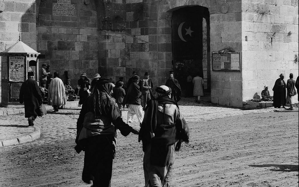 Exact location unknown, men walking towards Jerusalem's Old City. A Turkish flag visible in the gate shows that it is the Ottoman era. (Unknown)