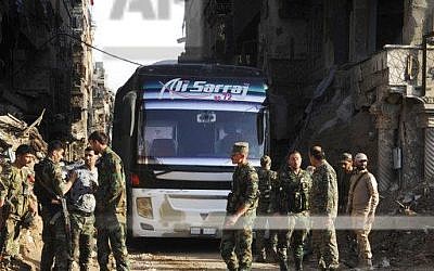 In this photo released on April 30, 2018, by the Syrian official news agency SANA, Syrian government forces gather in front of a bus carries al-Qaida-linked fighters during an evacuation from the Palestinian refugee camp of Yarmouk, near Damascus, Syria. (SANA via AP)