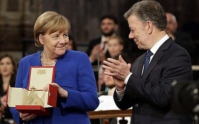 German Chancellor Angela Merkel, left, flanked by Colombian President Juan Manuel Santos, holds the St. Francis lamp peace prize she received by Father Mauro Gambetti during a ceremony inside Assisi's Basilica, Italy, Saturday, May 12, 2018. (AP Photo/Alessandra Tarantino)