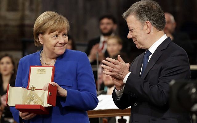 German Chancellor Angela Merkel, left, flanked by Colombian President Juan Manuel Santos, holds the St. Francis lamp peace prize she received by Father Mauro Gambetti during a ceremony inside Assisi's Basilica, Italy, Saturday, May 12, 2018. (AP Photo/Alessandra Tarantino) German Chancellor Angela Merkel, left, flanked by Colombian President Juan Manuel Santos, holds the St. Francis lamp peace prize she received by Father Mauro Gambetti during a ceremony inside Assisi's Basilica, Italy, Saturday, May 12, 2018. (AP Photo/Alessandra Tarantino)
