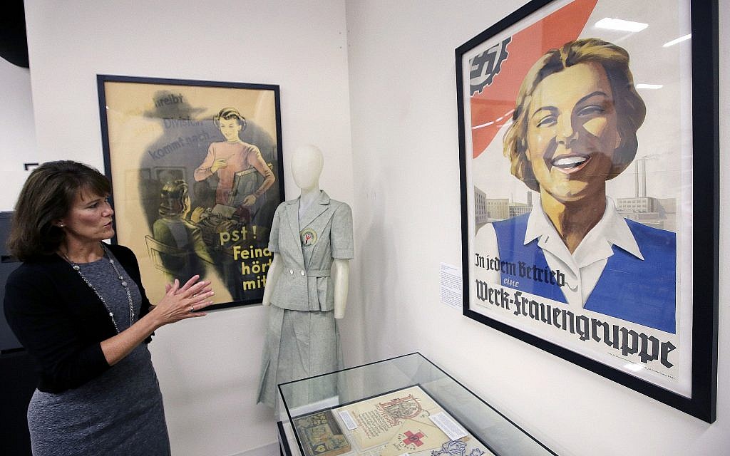 In this Monday, May 21, 2018, photo, Sue Wilkins, director of education at The International Museum of World War II, in Natick, Mass., stands near a 1933 propaganda poster, right, that praised the Nazi organization German Labor Front, which was created after the Nazis eliminated trade unions. (AP Photo/Steven Senne)